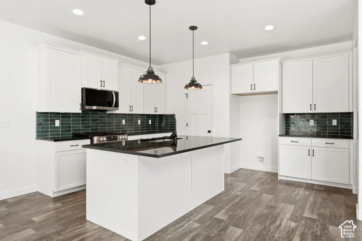 Kitchen featuring white shaker cabinetry, dark countertops, a dark tile backsplash, stainless steel appliances, and wood-finish flooring