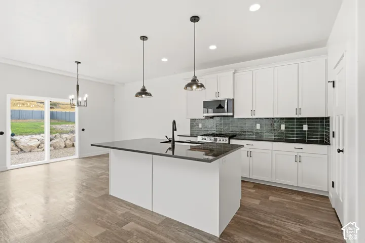 Kitchen with white cabinetry, dark countertops, a tile backsplash, and a center island with a sink