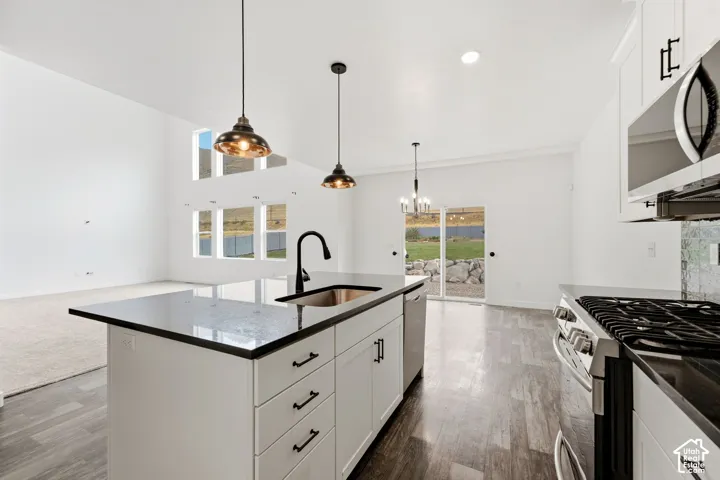 Kitchen island featuring a stainless steel sink and matte black faucet, pendant lighting, stainless steel appliances, wood-finish flooring, and a sliding glass door