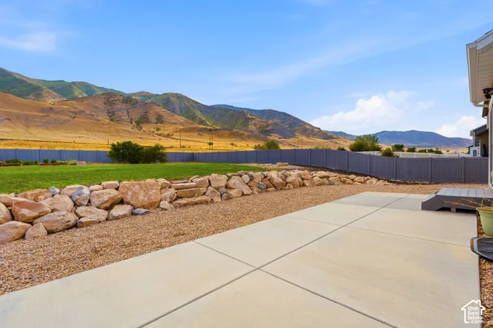 Expansive backyard featuring a concrete patio, composite deck, gravel landscaping, a rock retaining wall, and a manicured lawn