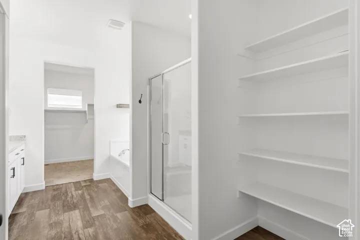 Spacious bathroom featuring wood-finish flooring, a glass-enclosed shower, a built-in tub, and extensive built-in shelving