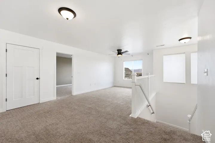 Carpeted upper-level room with a ceiling fan, window, and white paneled doors