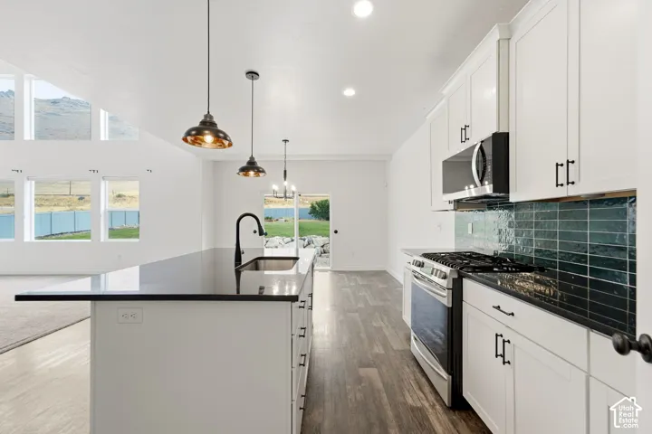 Kitchen featuring white cabinetry, dark countertops, a tile backsplash, stainless steel appliances, and a central island with a sink