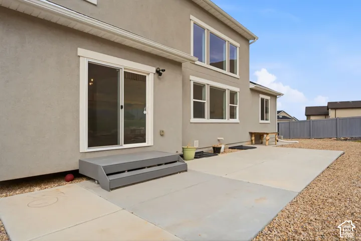 Stucco exterior with multiple windows, a sliding glass door, composite steps, and a concrete patio