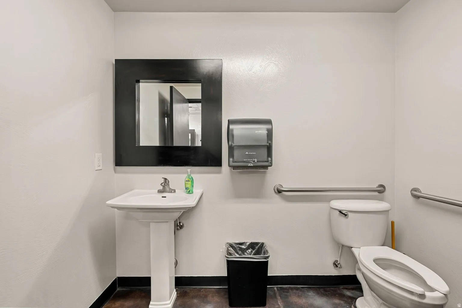Pedestal sink with chrome faucet, framed mirror, wall-mounted paper towel dispenser, and grab bars