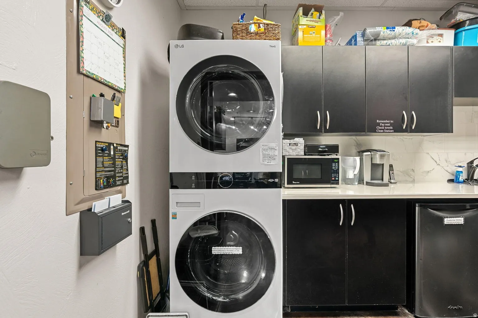 Stackable laundry appliances, black cabinetry, white countertops, and white tile backsplash