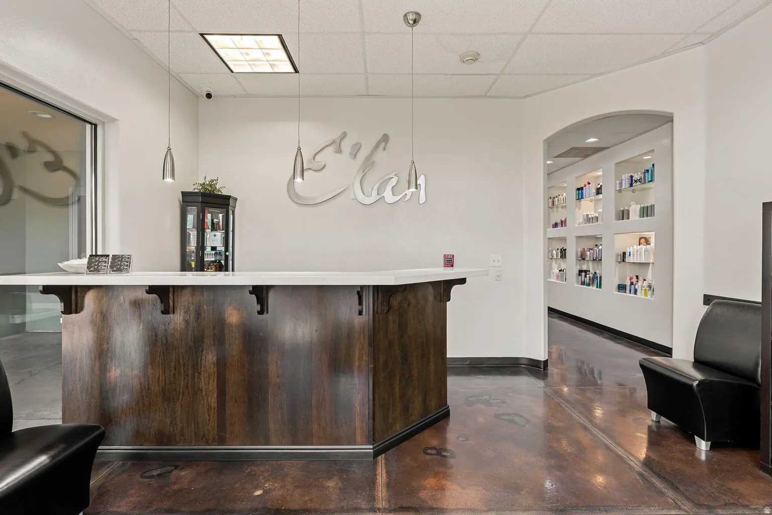 Reception area with a polished concrete floor, a built-in wood-finish reception desk with a light-colored countertop, and recessed display shelving