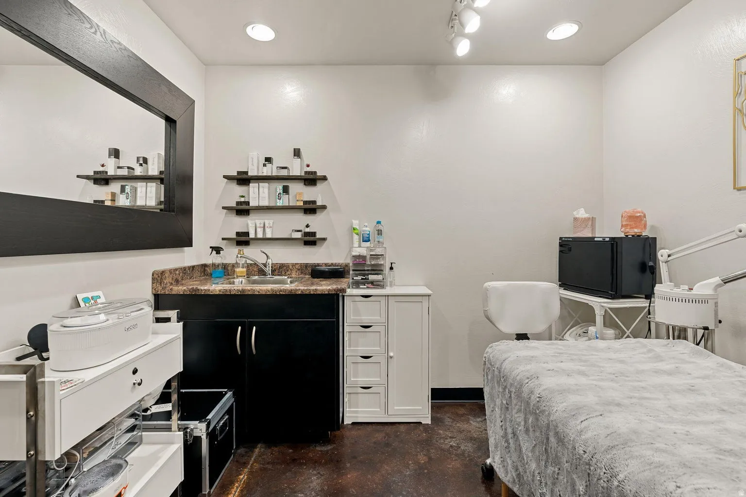 Recessed and track lighting illuminate a sink with a dark countertop and cabinetry