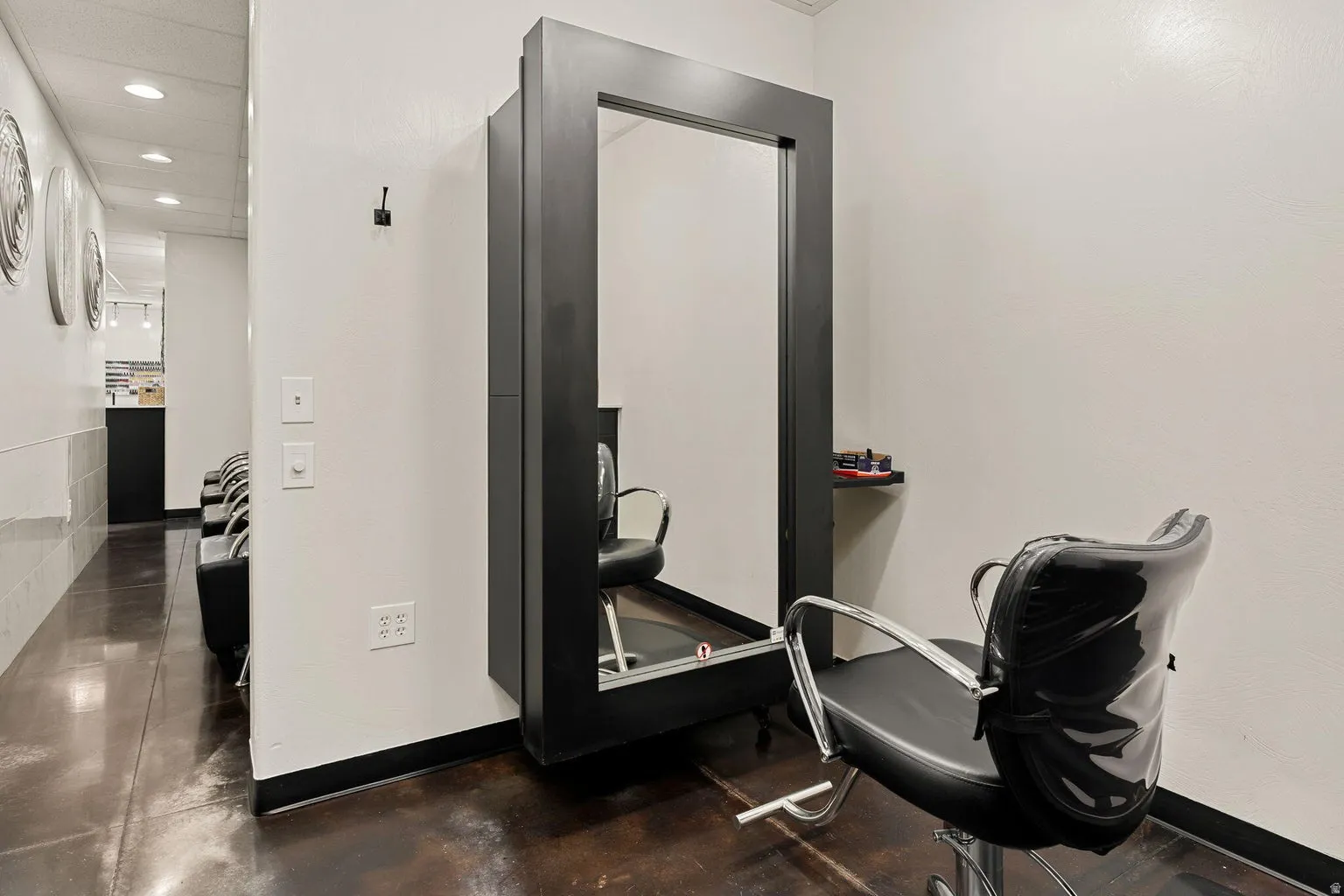 Wall-mounted mirror station with a dark frame, sleek dark flooring, and recessed ceiling lighting
