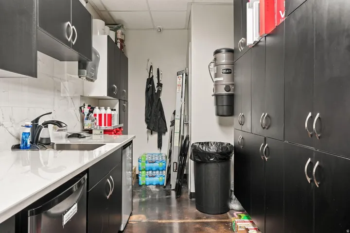 Sleek black cabinetry with chrome hardware, white solid surface countertop, stainless steel sink, and a built-in compact refrigerator