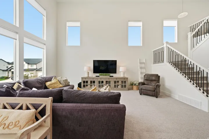Two-story volume ceiling, multi-pane windows, light-toned carpeting, modern open staircase with metal balusters, and a built-in media console with glass panel doors