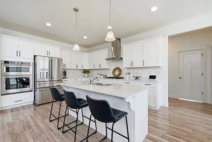White shaker cabinetry, stainless steel appliances, central island with seating, pendant lighting, and wood-finish flooring