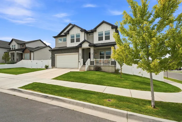 Modern two-story home featuring a covered porch, attached garage, and a fenced yard with mature trees