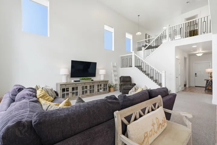 Vaulted ceiling great room with upper-level windows, a staircase featuring decorative metal balusters, and an entryway with wood-finish flooring