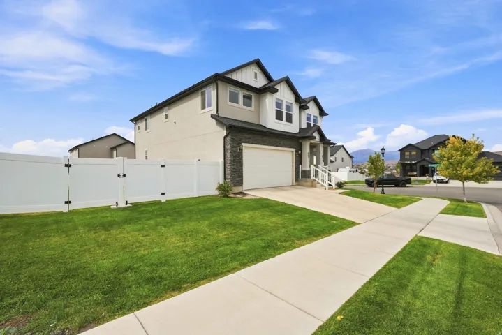 Two-story residence featuring a stone and stucco exterior, attached garage, concrete driveway, and a fenced yard with a sidewalk