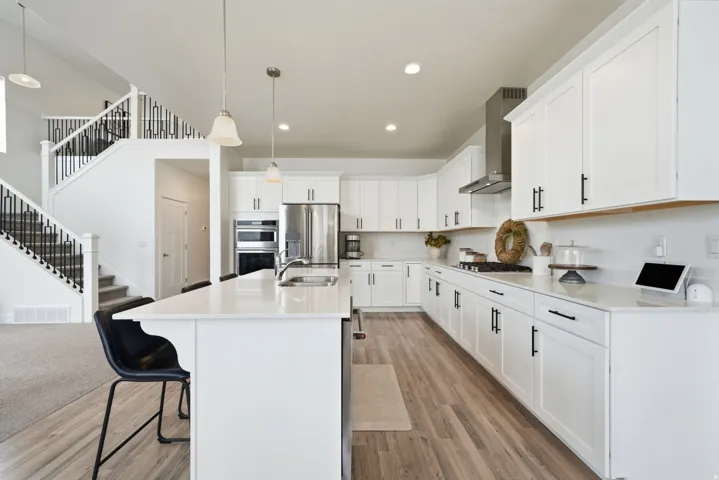 Kitchen featuring white cabinetry, stainless steel appliances, a center island with sink, and wood-finish flooring