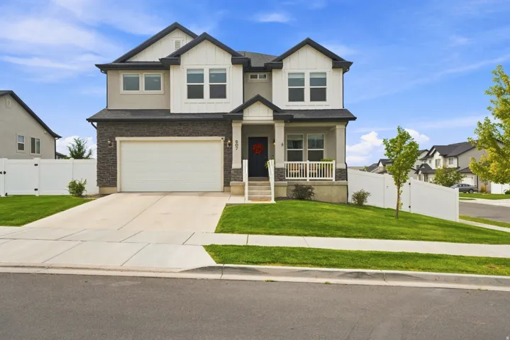Two-story residence featuring a two-car garage, stone and siding exterior, front porch with white railing, and a fenced yard