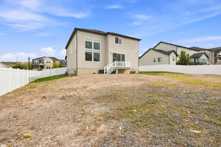 Rear exterior with stucco finish, white vinyl fencing, an upper-level deck, and sliding glass doors
