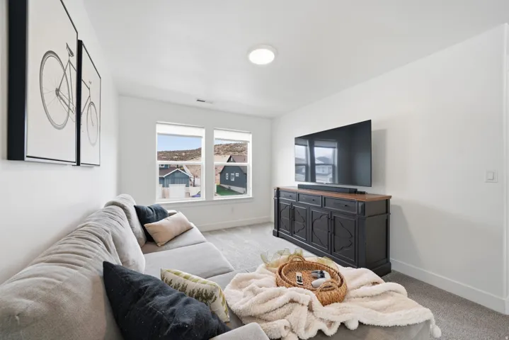 Plush carpeting throughout with bright white walls, featuring dual windows and a built-in media console with a wood-finish top