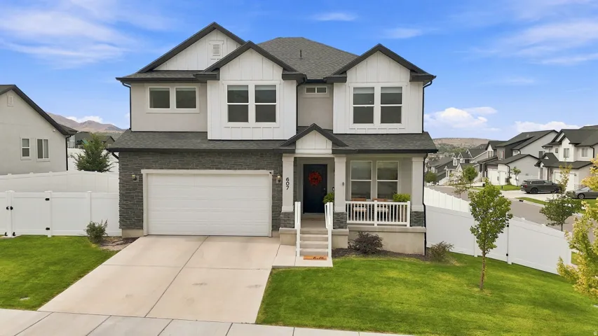 Modern two-story residence featuring a stone and stucco exterior, an attached two-car garage, a covered front porch, a concrete driveway, and a fenced yard