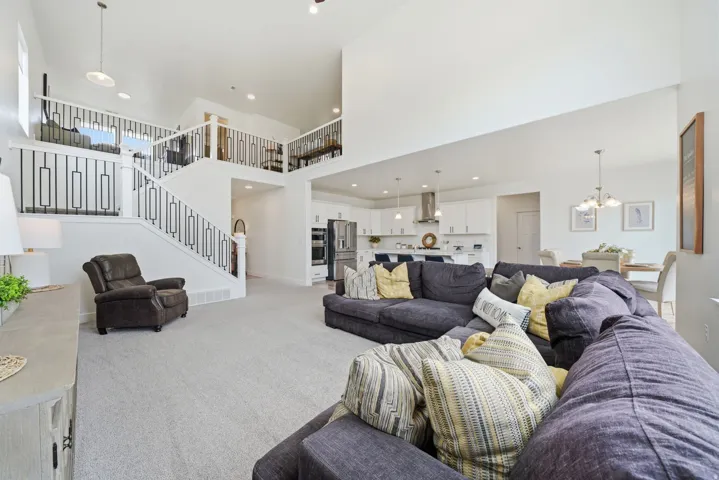 Two-story ceiling, open-concept layout, modern stair railing, white kitchen cabinetry, and stainless steel appliances