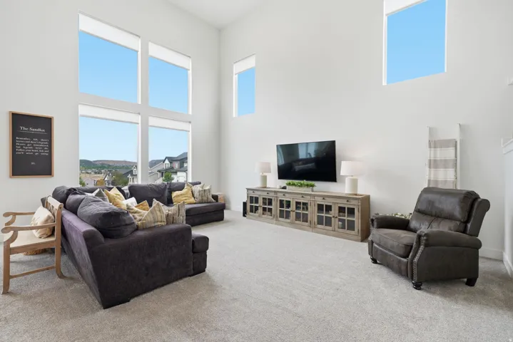 Two-story white walls with high ceilings, multiple large windows, and neutral carpet flooring