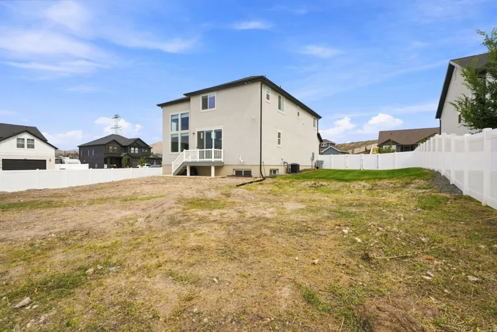 Rear exterior featuring a ground-level patio, white railing staircase, multiple windows, and a fully fenced backyard