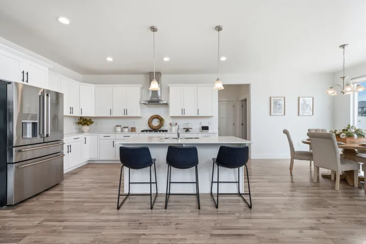 White cabinetry with matte black hardware, stainless steel appliances, a kitchen island with pendant lighting, stone countertops, and wood-finish flooring