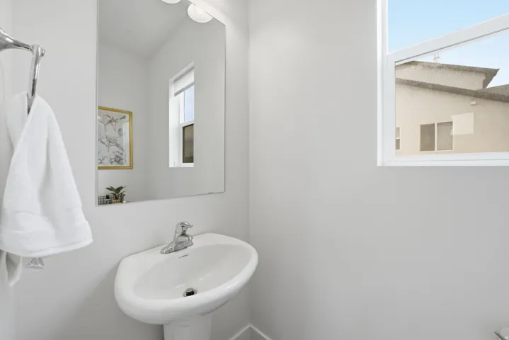 Pedestal sink with chrome faucet, wall-mounted mirror, and overhead vanity lighting