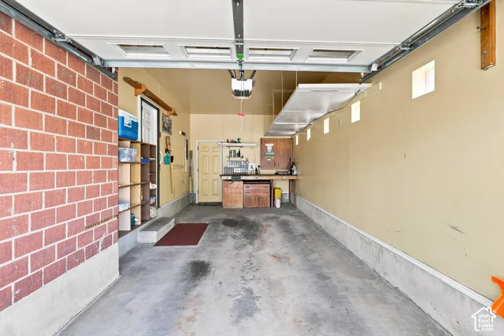 Attached garage with concrete flooring, exposed brick wall, built-in shelving, and a wood-finish workbench