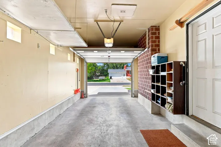 Attached garage with concrete flooring, multiple high-set windows, and an interior brick wall accent