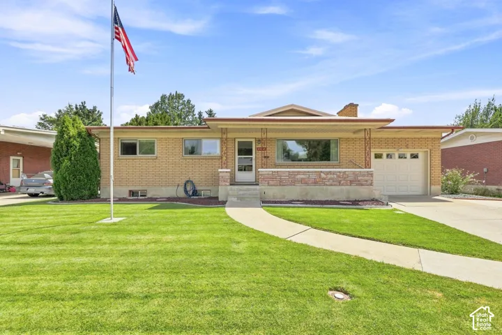 Brick exterior with a covered front porch featuring stone accents, an attached garage, a paved driveway, and a concrete walkway