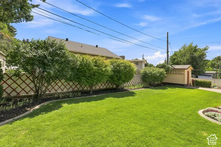 Expansive green lawn with a decorative lattice fence, mature shrubs, a defined garden bed, and an exterior storage shed