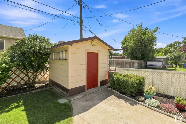 Detached storage shed with a pitched roof, concrete pad, and fenced yard with mature trees