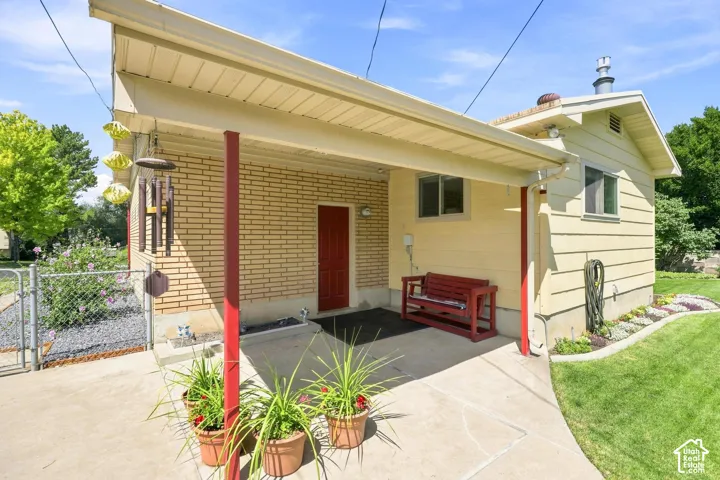 Covered patio with concrete slab, brick exterior, and a red entry door