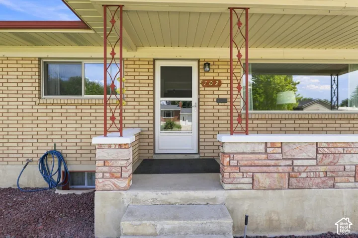 Welcoming front entrance featuring a brick and stone exterior with decorative red metal support columns, a recessed entryway with a white-framed glass door, and a concrete foundation with stepped approach