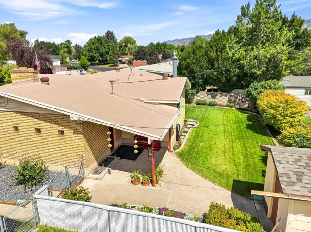 Expansive rear yard with a manicured lawn, tiered retaining wall, mature trees, and a concrete patio