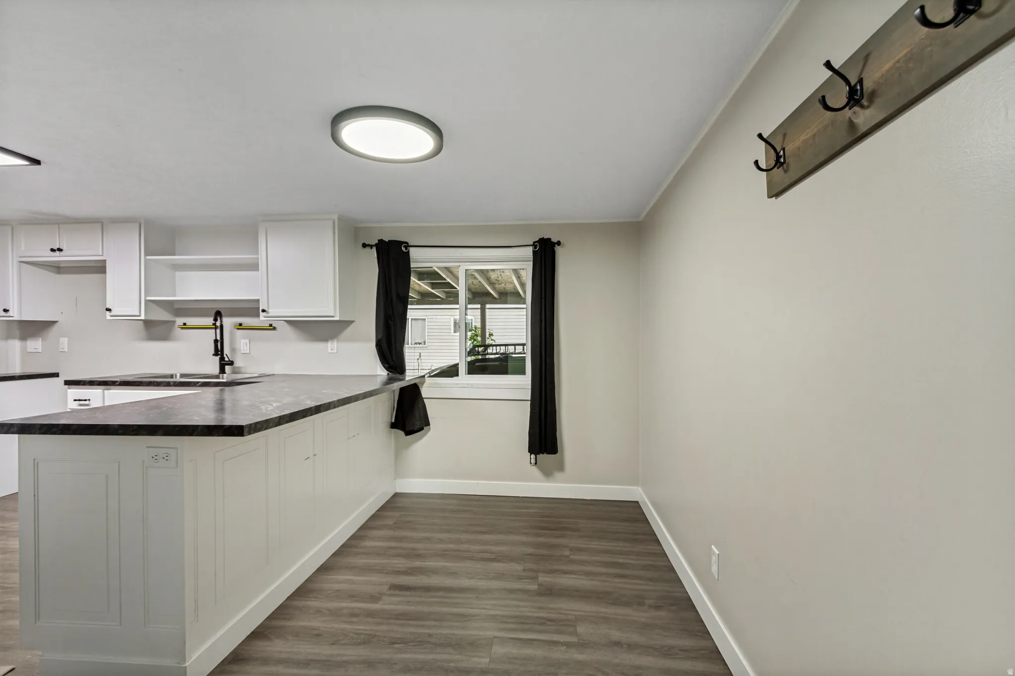 Kitchen featuring white cabinetry, dark countertops, a single basin sink with a gooseneck faucet, and wood-finish flooring