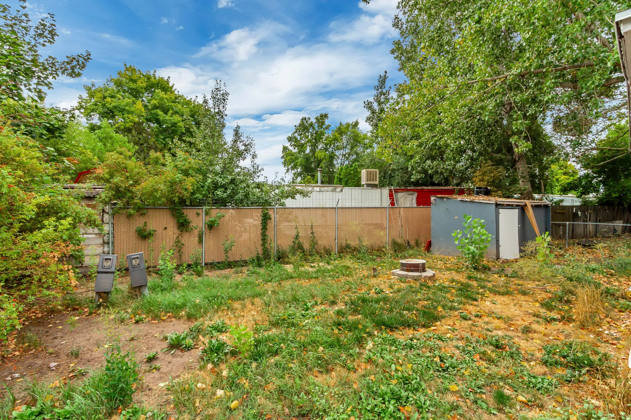 Expansive yard featuring mature trees, partial fencing, and a detached storage shed