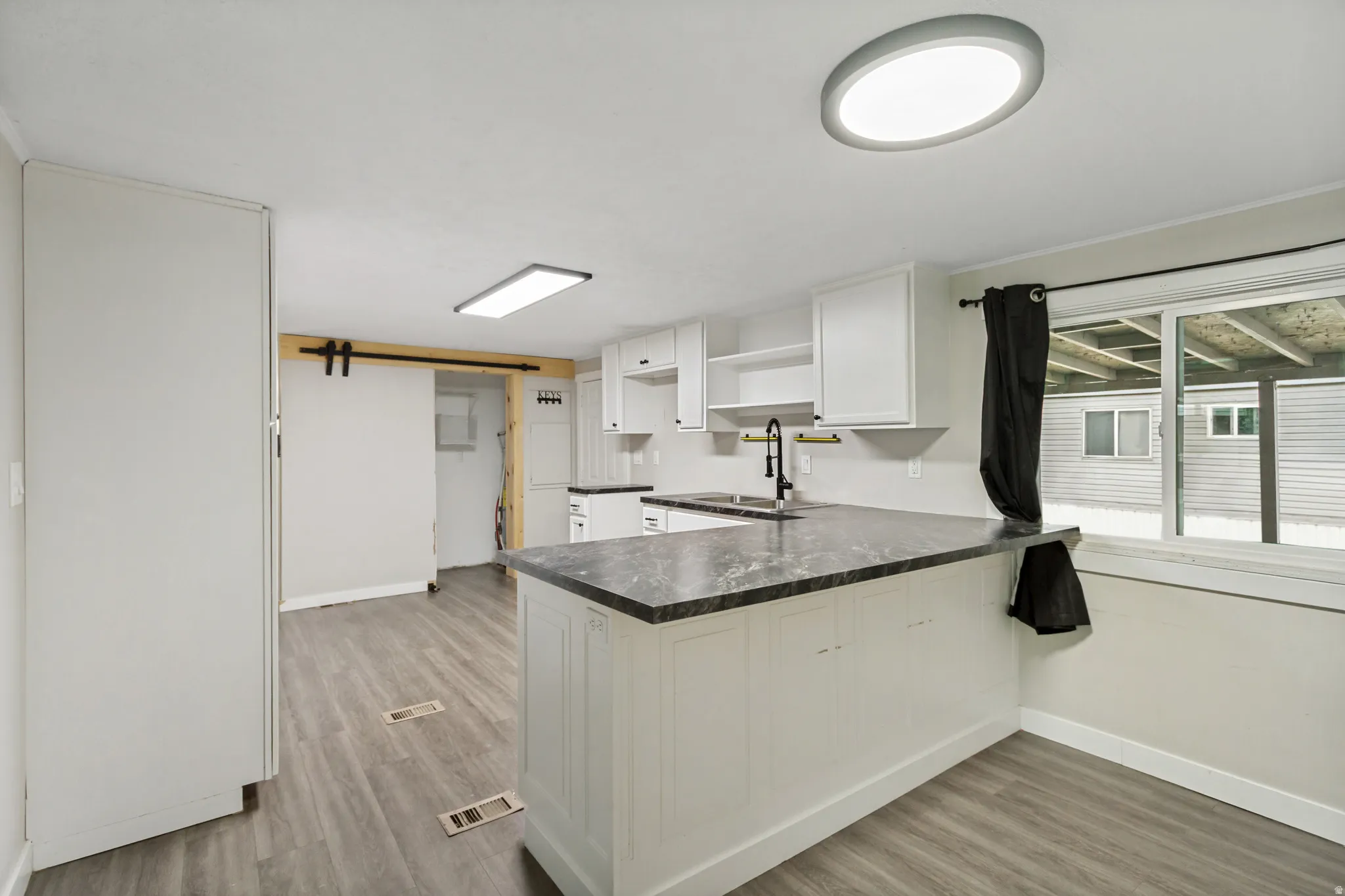 Kitchen featuring a breakfast bar, wood-finish flooring, white cabinetry, dark countertops, and a sliding barn door