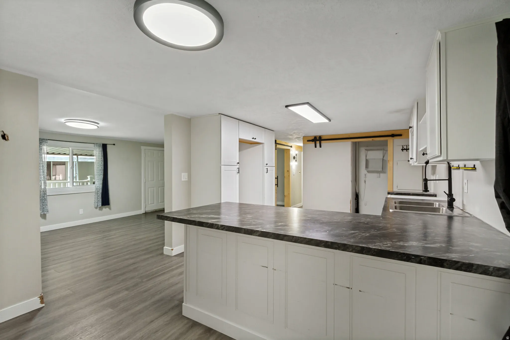 Kitchen island with dark countertop, white cabinetry, undermount sink, and black hardware
