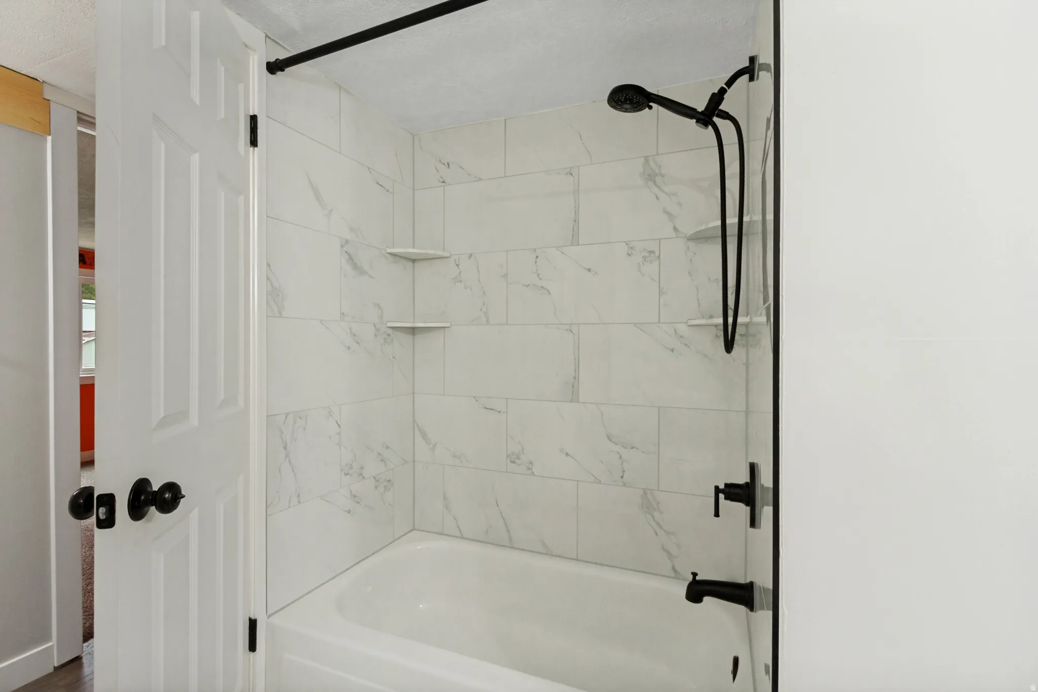Bathtub with subway tile surround, corner shelving, and matte black fixtures including a shower head and faucet
