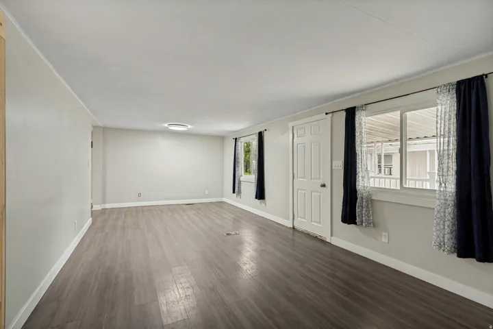 Spacious room featuring wood-finish flooring, light neutral wall tones, multiple windows, a white paneled door, and a flush-mount ceiling light