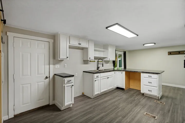 Modern kitchen featuring white cabinetry, dark countertops, a built-in sink with a black gooseneck faucet, and wood-finish flooring