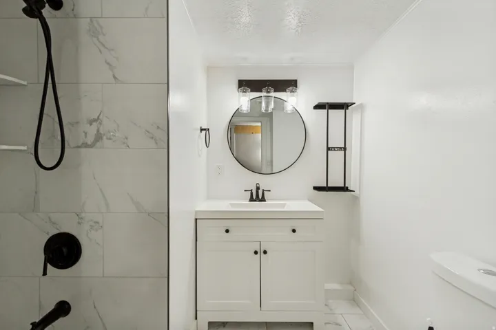 Bathroom featuring a white vanity with an integrated sink, a round mirror, and a three-light fixture