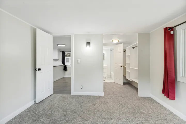 Neutral gray wall paint with white trim, gray carpet, built-in closet shelving, and a wall-mounted sconce