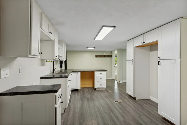 White cabinetry with black hardware, dark countertops, wood-finish flooring, and recessed lighting
