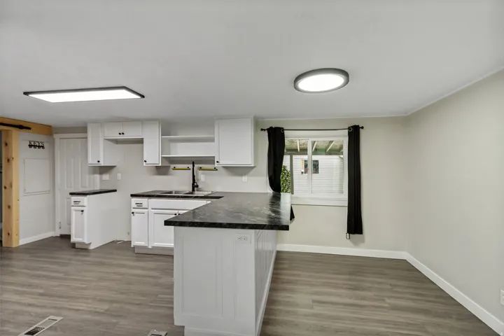 Modern kitchen featuring white cabinetry, dark countertops, wood-finish flooring, and a contemporary sink with a black faucet