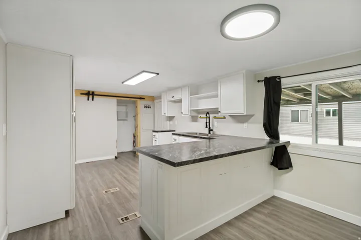 Kitchen featuring a breakfast bar, wood-finish flooring, white cabinetry, dark countertops, and a sliding barn door