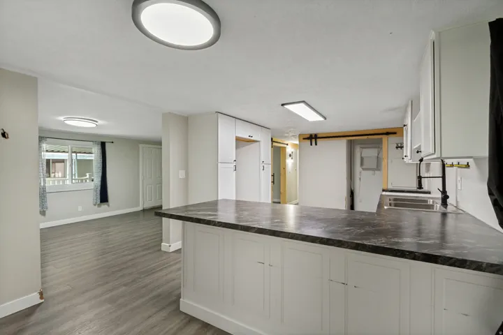 Kitchen island with dark countertop, white cabinetry, undermount sink, and black hardware